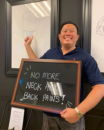 A man holds a sign that reads, "NO MORE NECK AND BACK PAINS!".