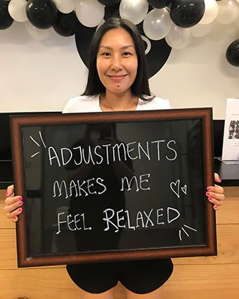 A woman holds a sign that reads, "Adjustments Makes Me Feel Relaxed".