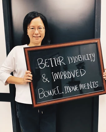 A woman holds a sign that reads, "BETTER MOBILITY & IMPROVED BOWEL MOVEMENTS".