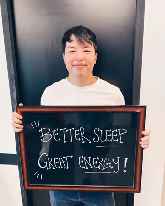 A man holds a sign that reads, "BETTER SLEEP GREAT ENERGY!".