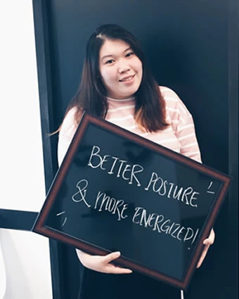 A woman holds a sign that reads, "BETTER POSTURE & MORE ENERGIZED!".