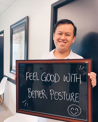 A man holds a sign that reads, "FEEL GOOD WITH BETTER POSTURE".