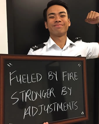 A man flexes his bicep and holds a sign reading "FUELED BY FIRE STRONGER BY ADJUSTMENTS".