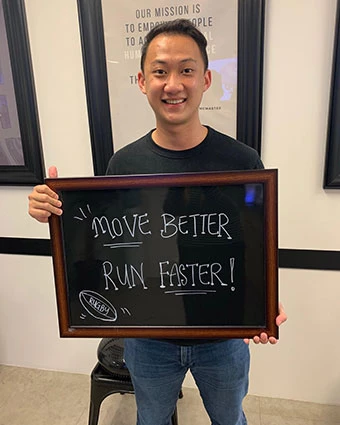 A man holds a sign that reads, "MOVE BETTER RUN FASTER!".